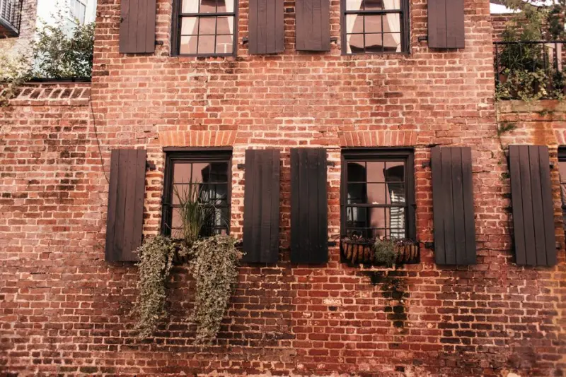 Vintage brick wall with wooden shutters and decorative plants in window boxes.